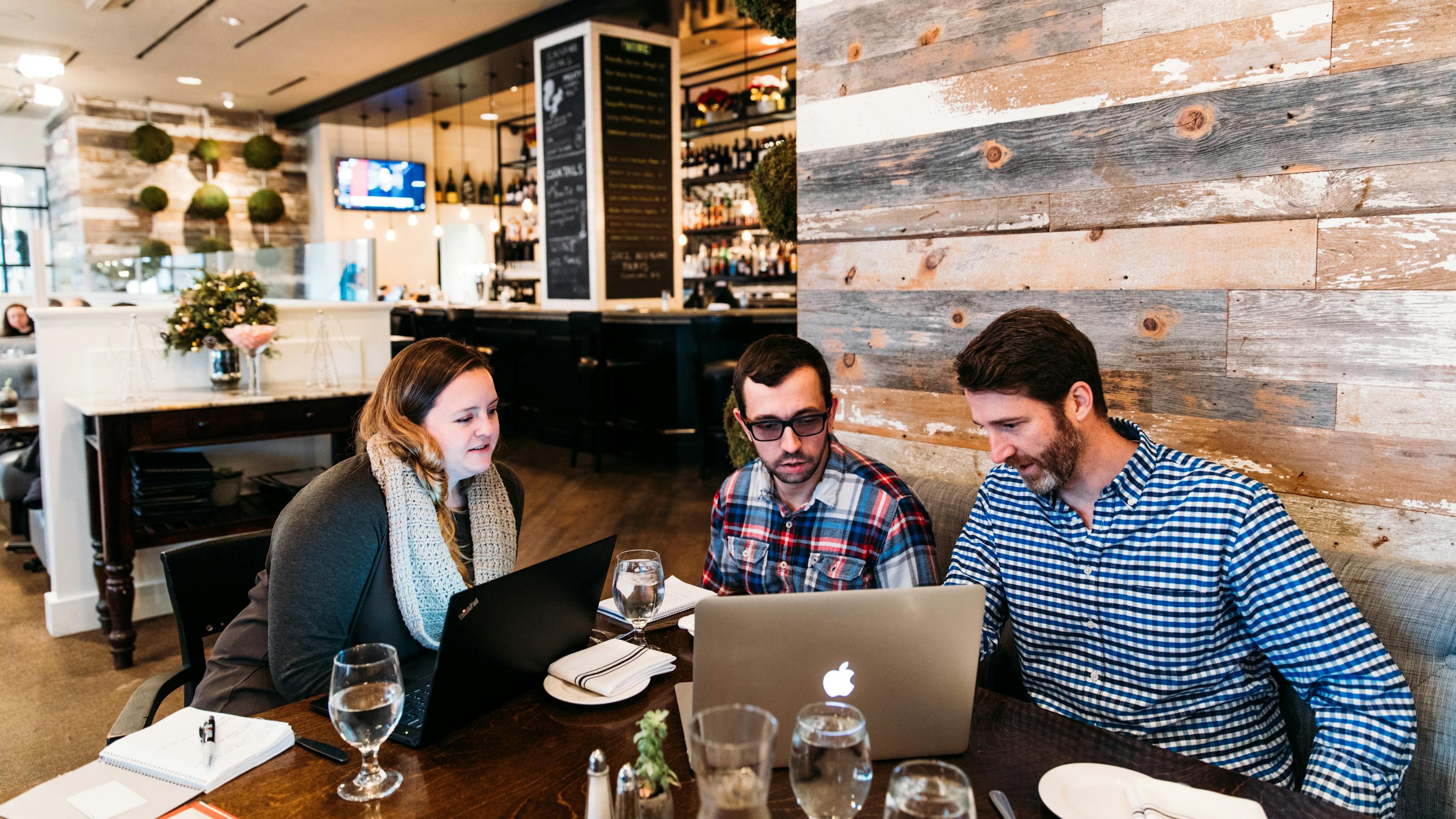 Three people sitting at a table at a restaurant looking at a laptop