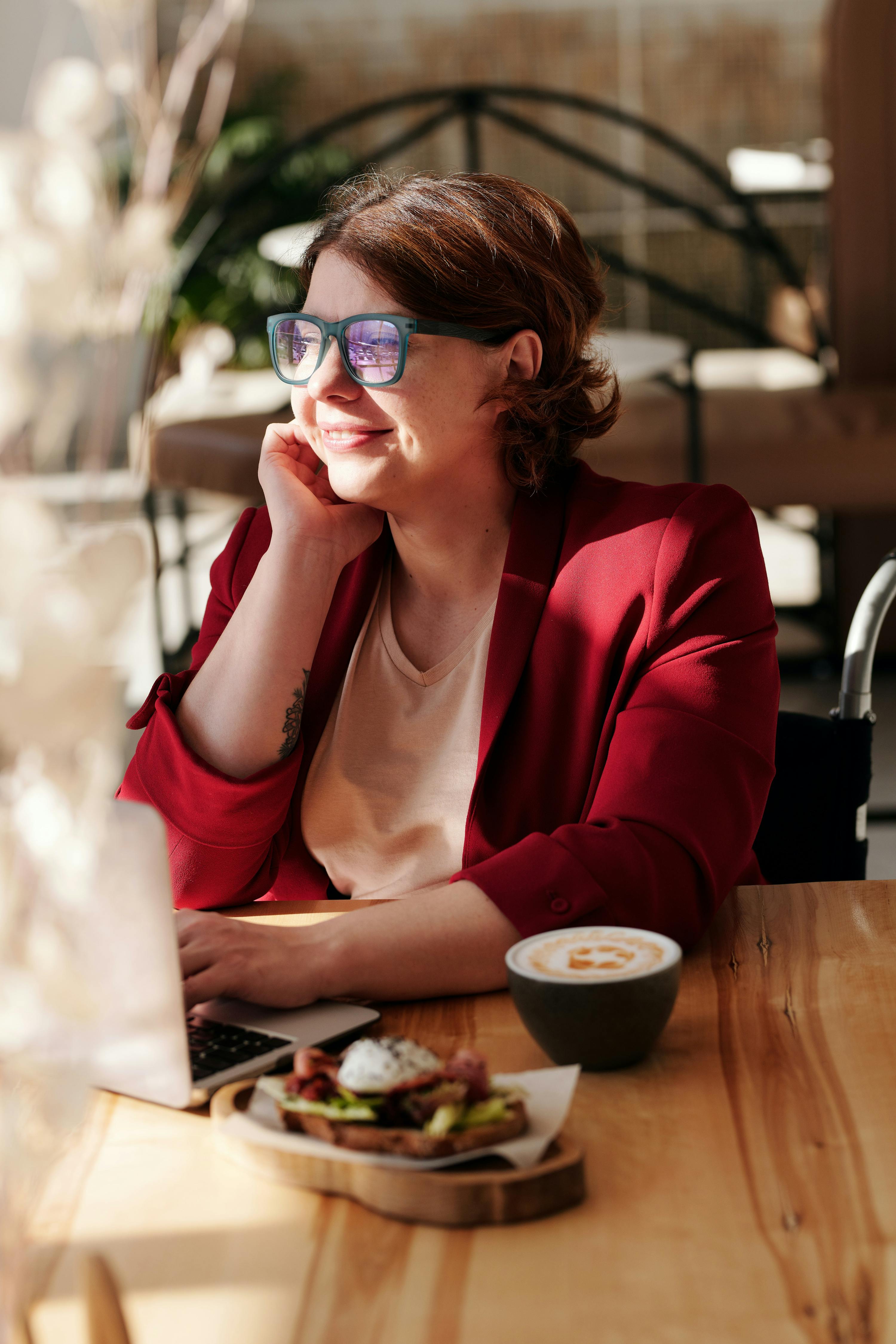 Woman wearing blue glasses using a laptop at a cafe with coffee and toast on the table