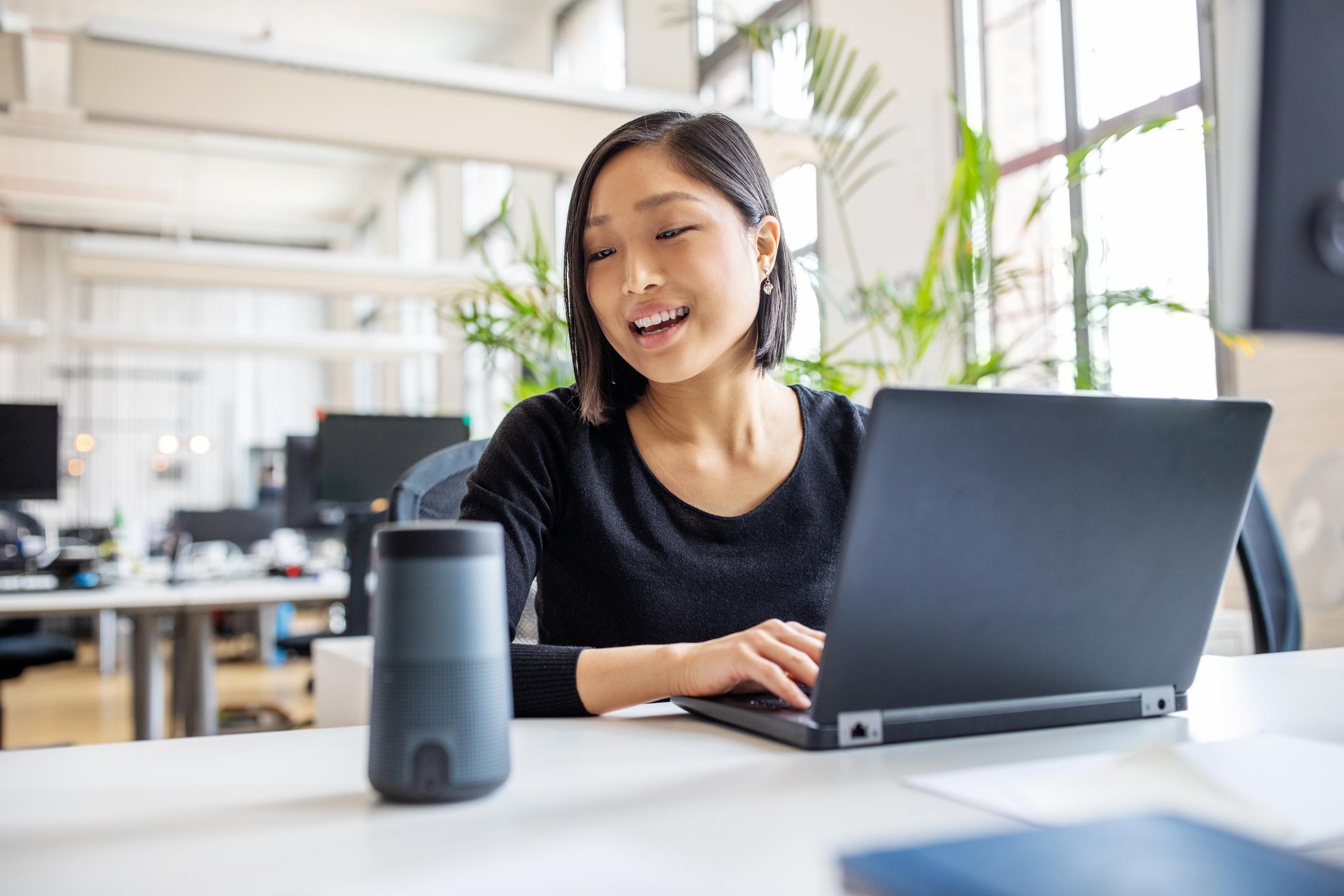 Woman using a laptop with a bluetooth speaker on her desk