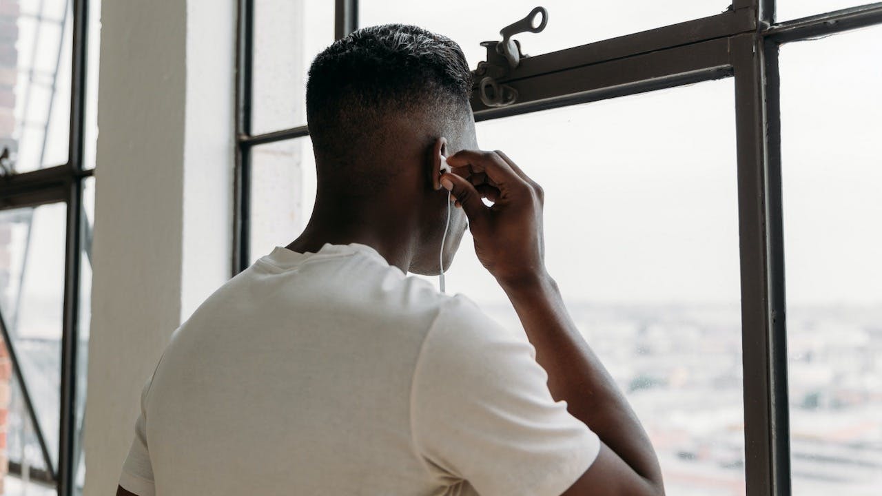 Man putting an earbud in his ear while looking out a window