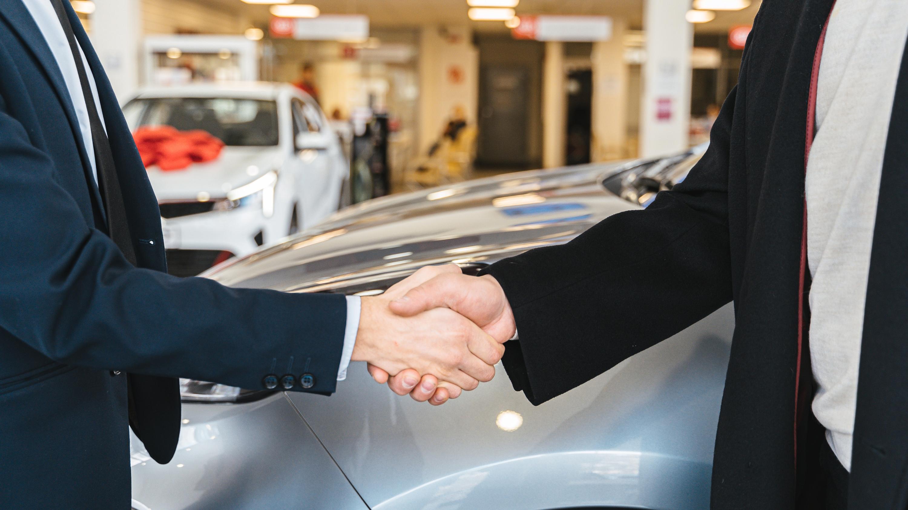 Two people shaking hands in front of a car in a dealership