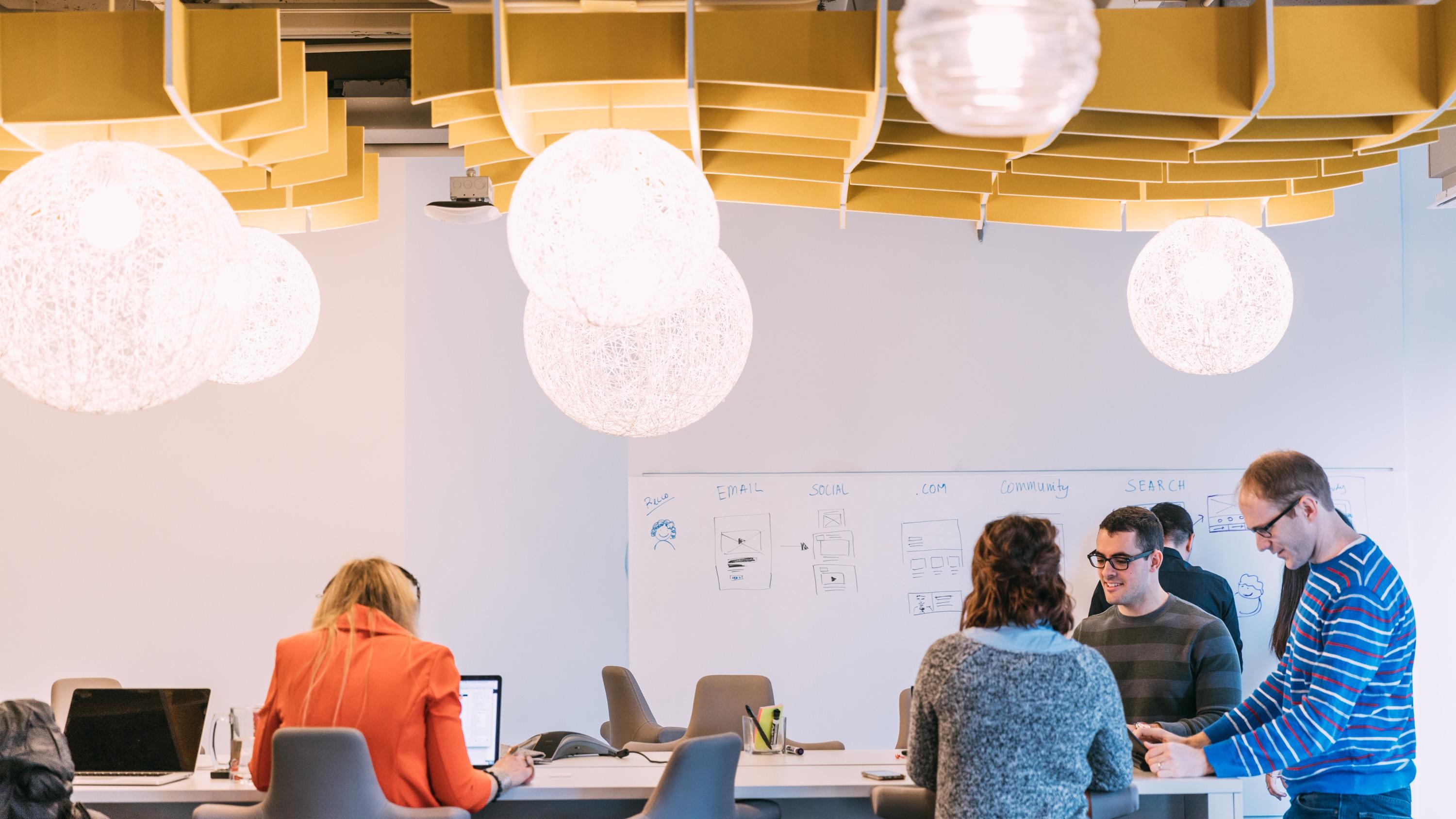 People gathered in a workspace with a whiteboard and spherical light fixtures