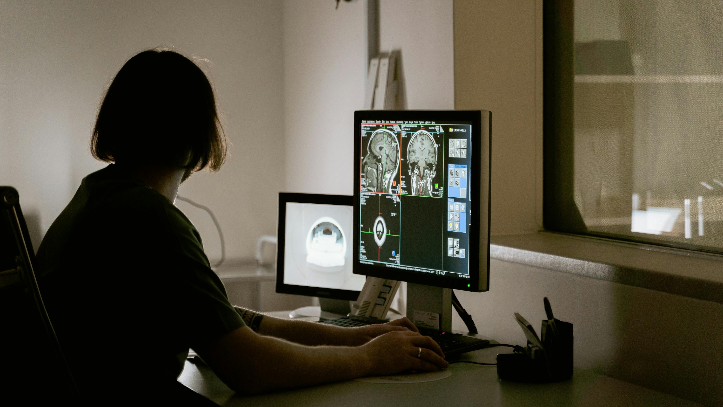Healthcare worker looking at brain scan images on two monitors