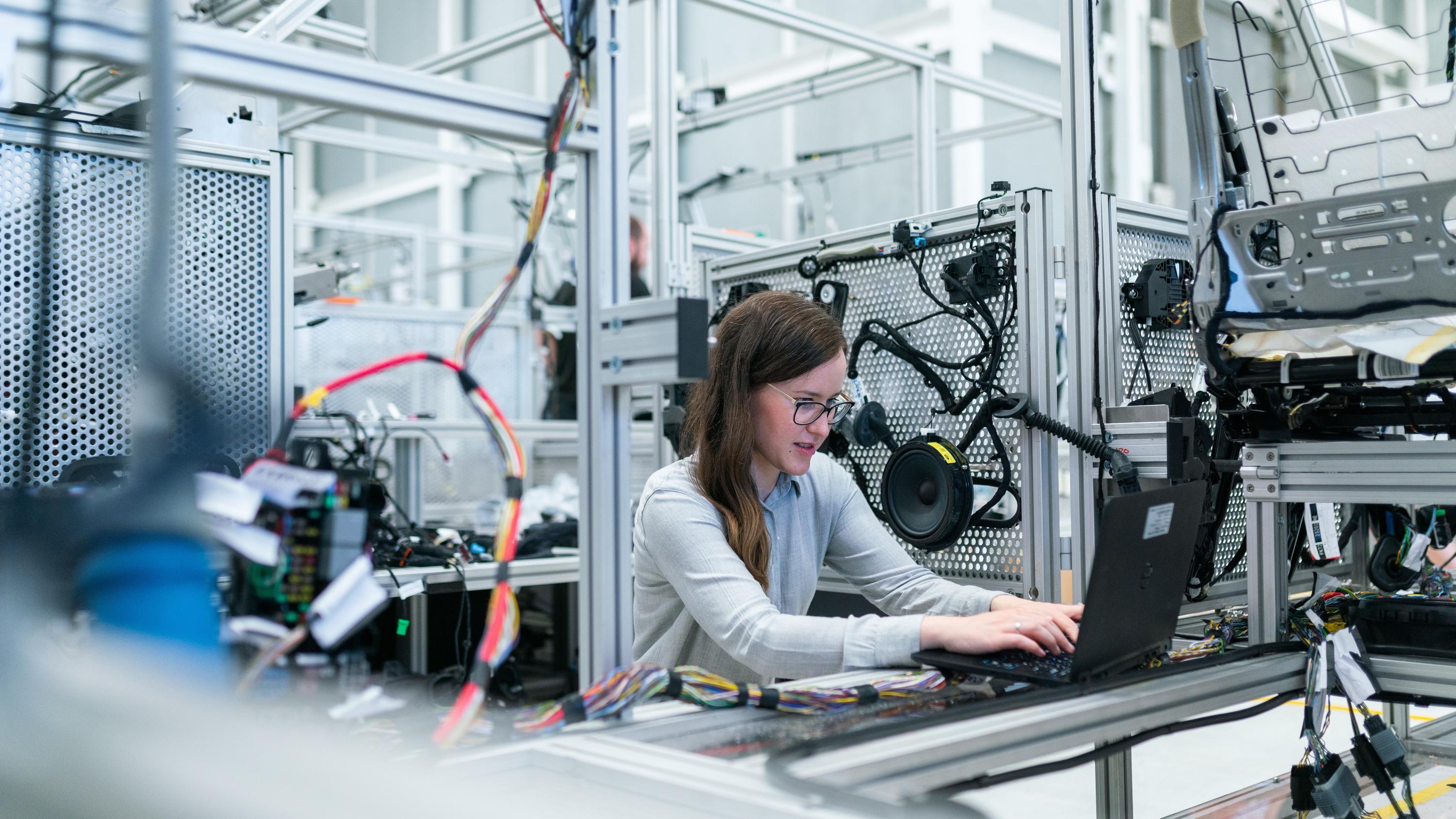 Woman working on a laptop surrounded by many wires and technology equipment