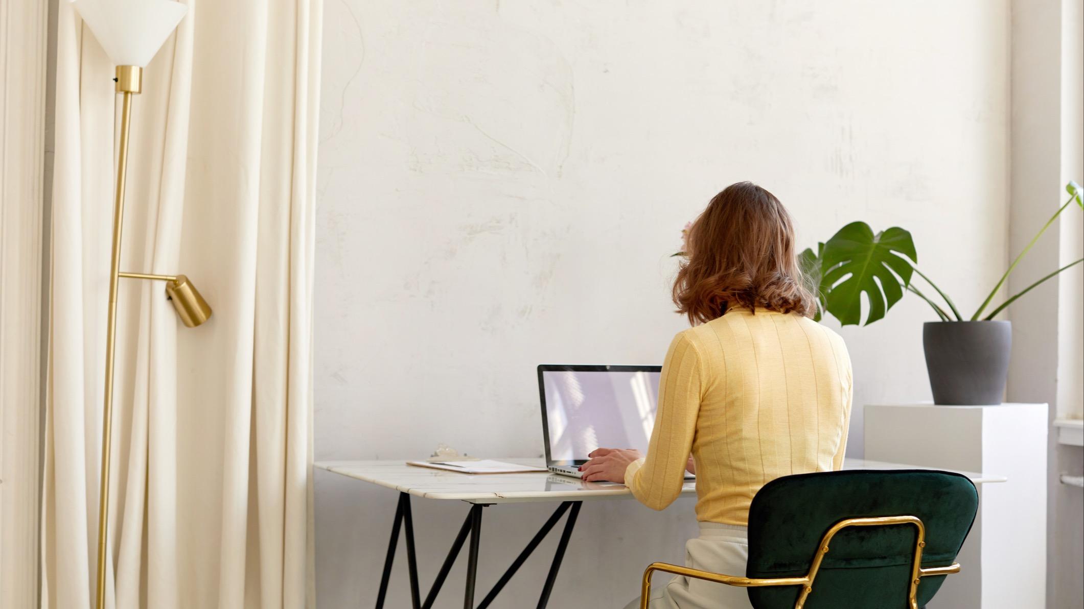 Woman using her laptop sitting at a desk in a white room