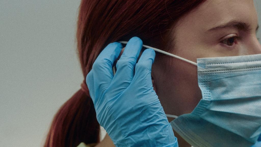 Woman wearing surgical gloves putting on a surgical mask