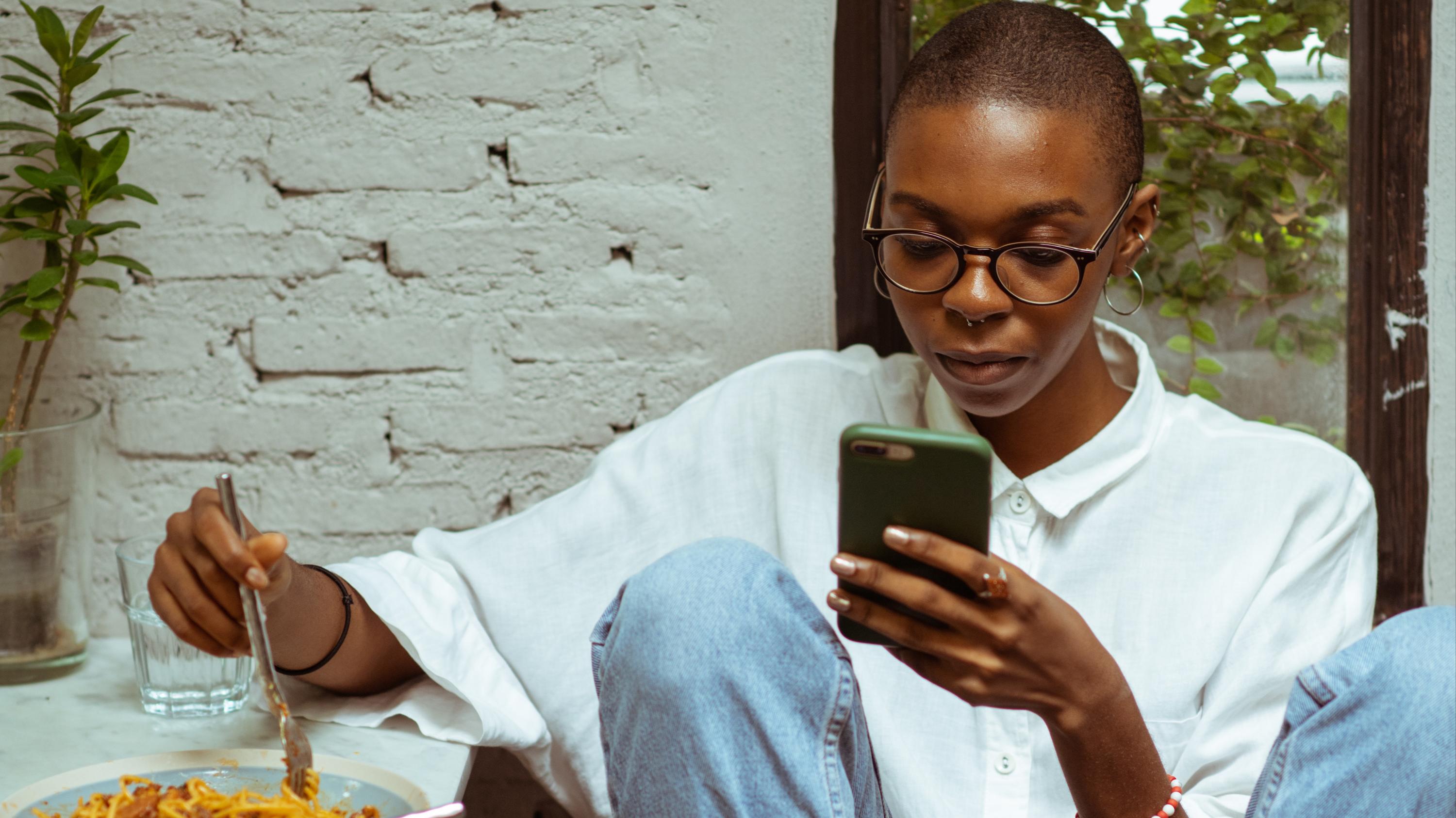 Woman sitting outside with a bowl of food using her smartphone