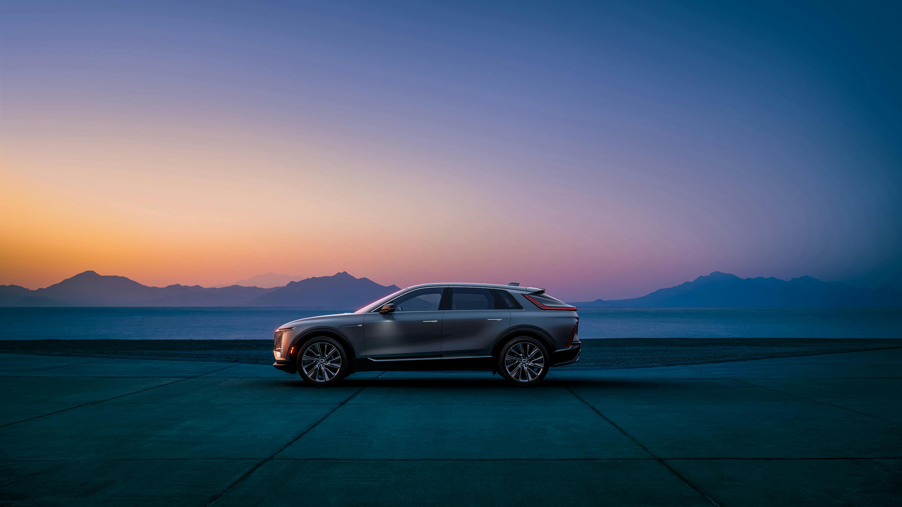 A Cadillac SUV in front of a sunset with mountains in the distance