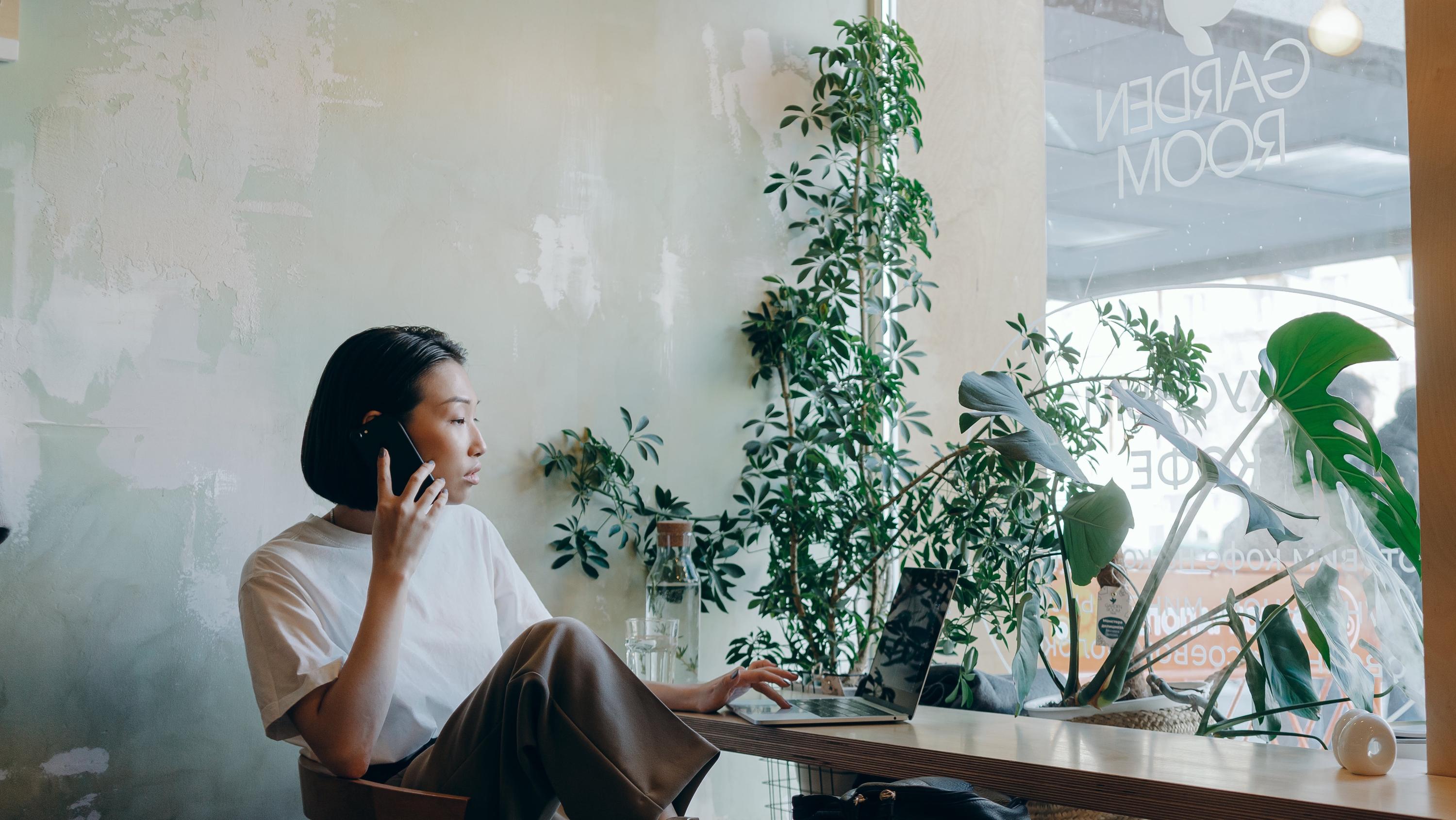 Woman on the phone in coffee shop looking at laptop