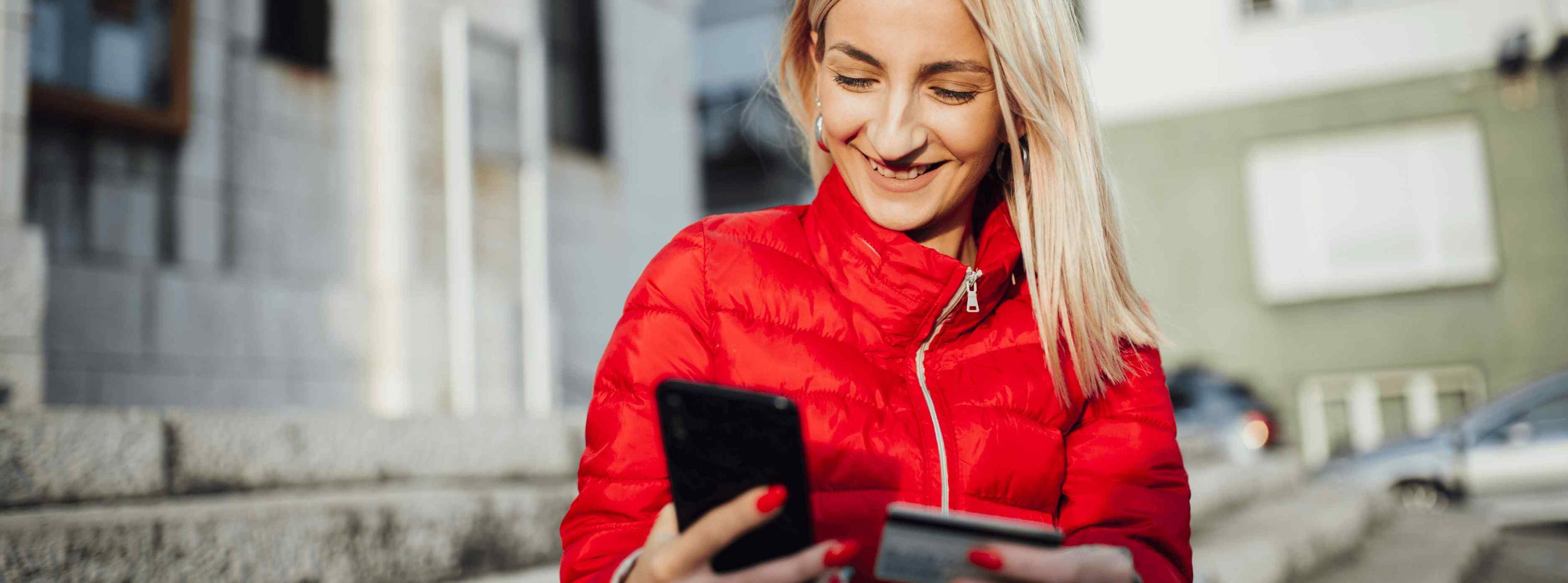 A woman smiling while looking at her mobile phone and credit card. An example of a customer experience.