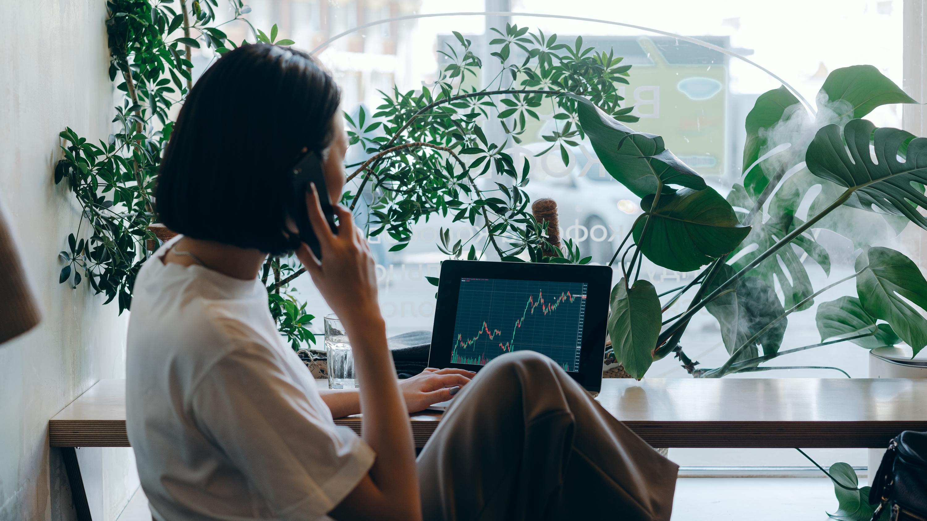 Woman on the phone while viewing stocks on her laptop