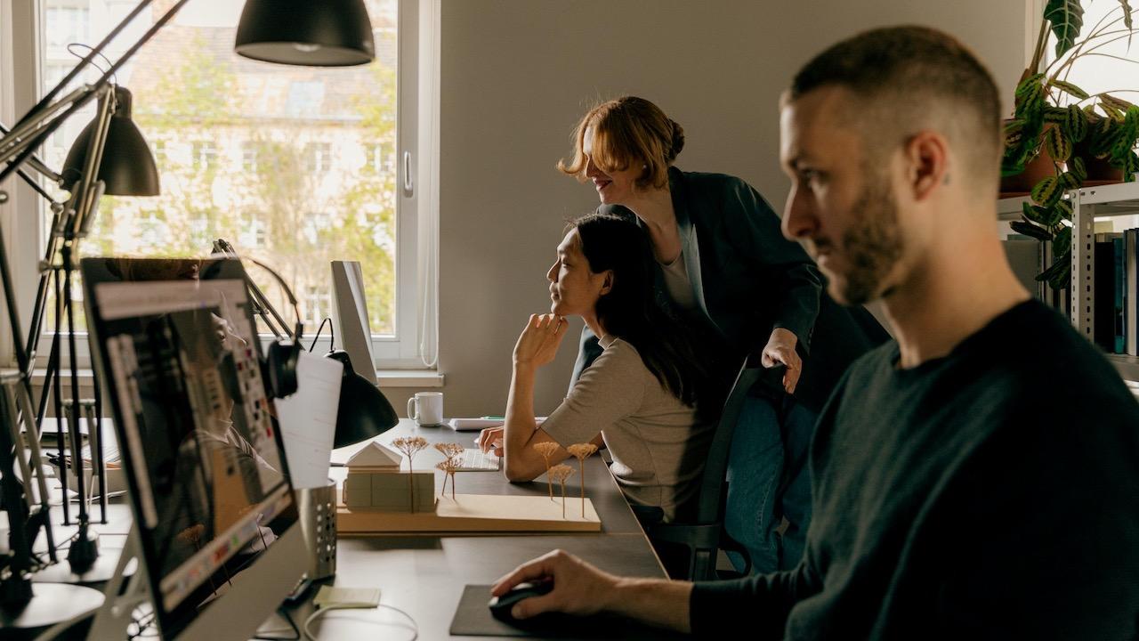 Three people working at a long table looking at computer screens